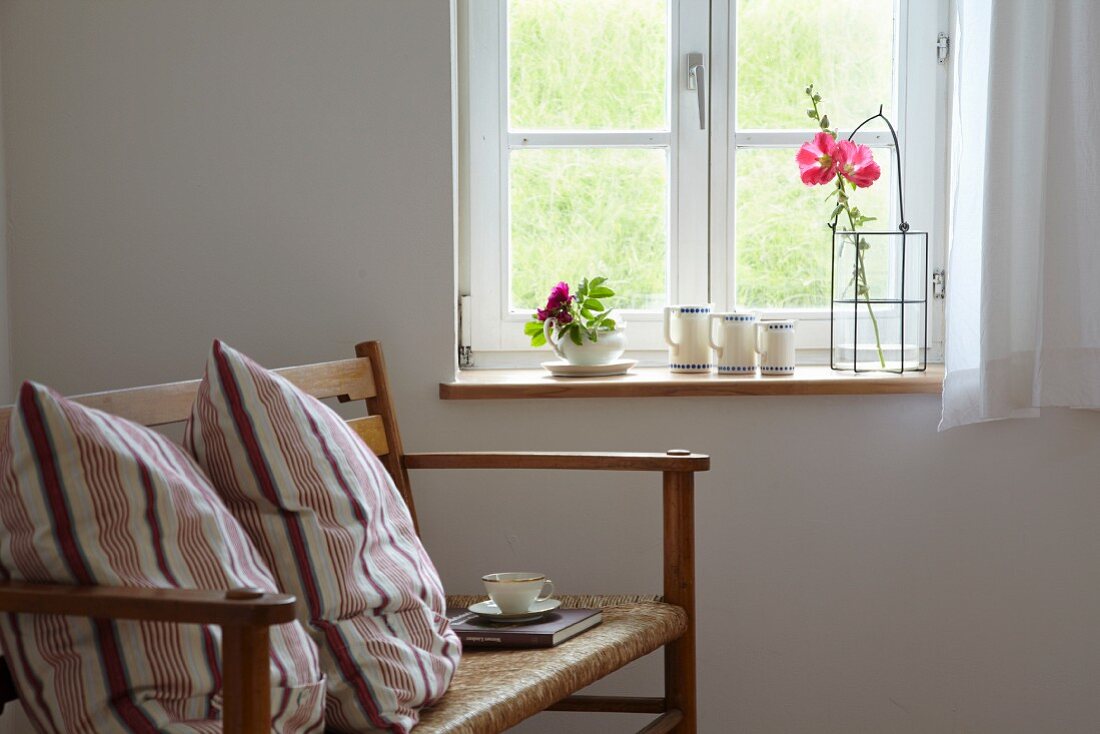 Holzbank mit Kissen und Teetasse beim Fenster