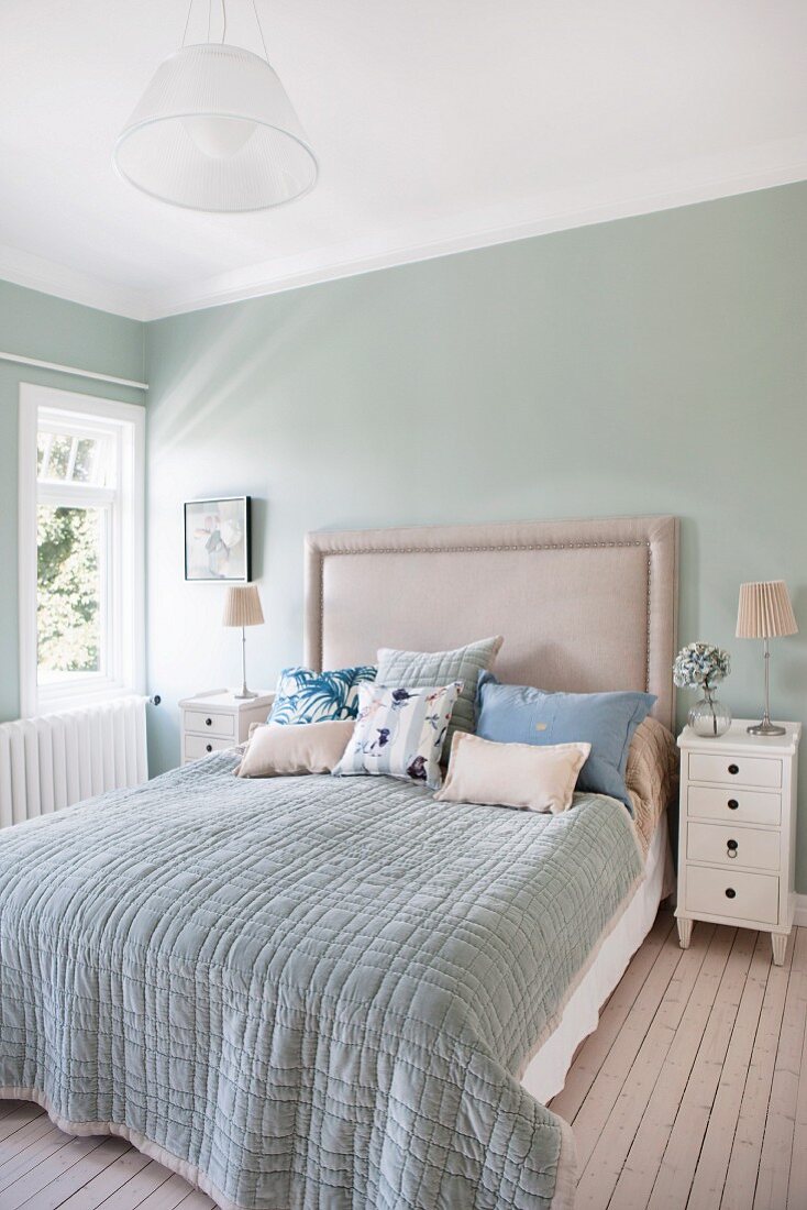 Doppelbett mit Polsterkopfteil an pastellgrüner Wand im Schlafzimmer