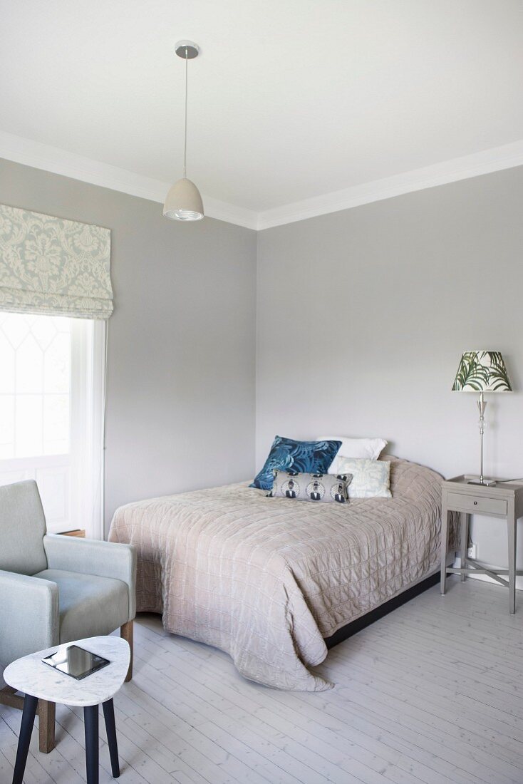 Doppelbett mit Plaid und Kissenstapel an pastellgrauer Wand in Schlafzimmerecke