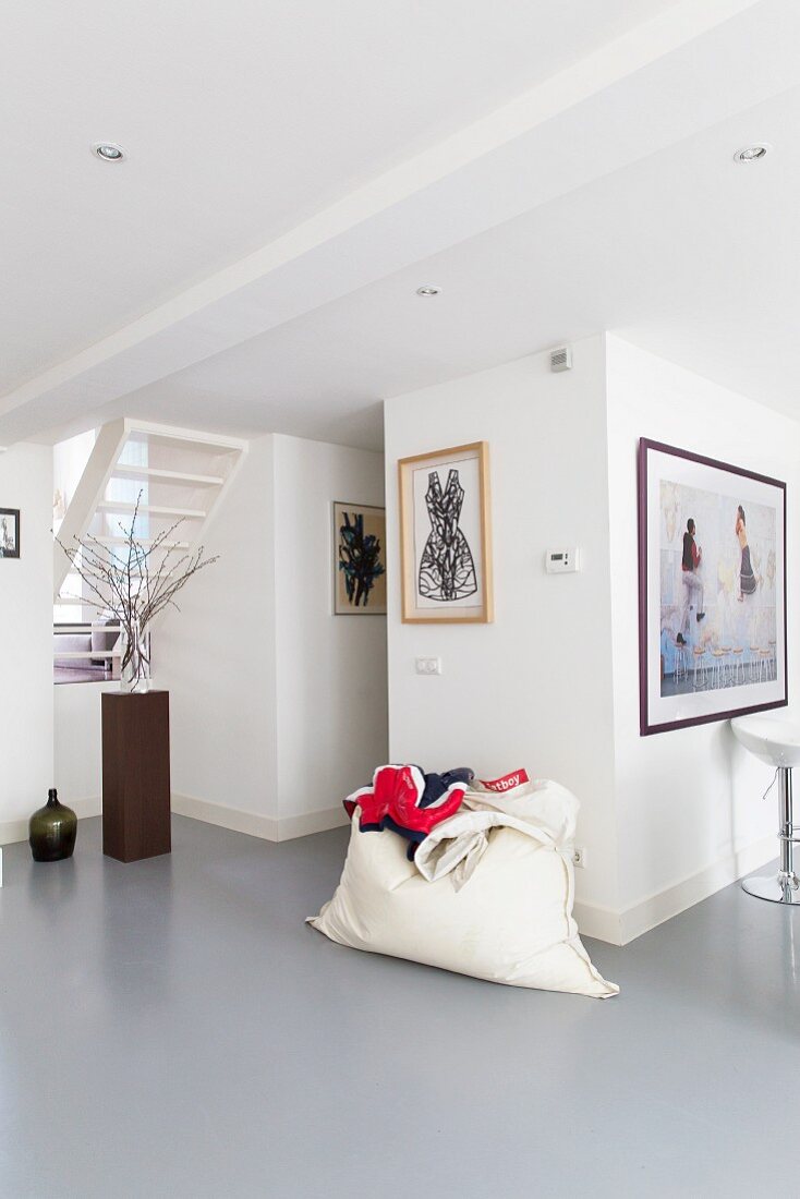 Moderner Wohnraum mit grauem Kunstharzboden, weisser Sitzsack vor Wand mit gerahmten Bildern