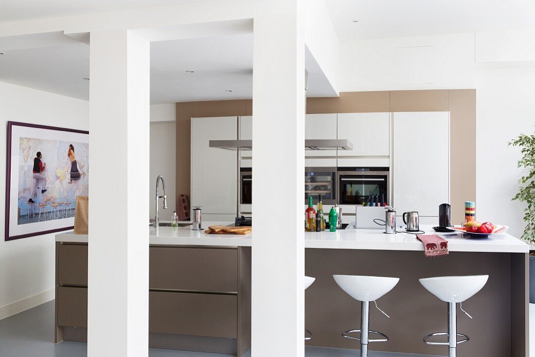 Offene Küche mit Kücheninsel, weiße Arbeitsplatte auf braunem Korpus, davor Barhocker in loftartigem Wohnraum