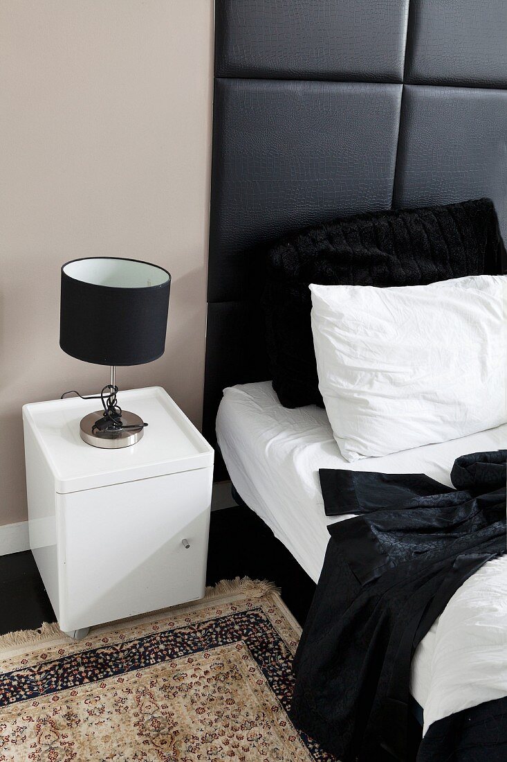 Table lamp with black lampshade on white bedside cabinet next to bed