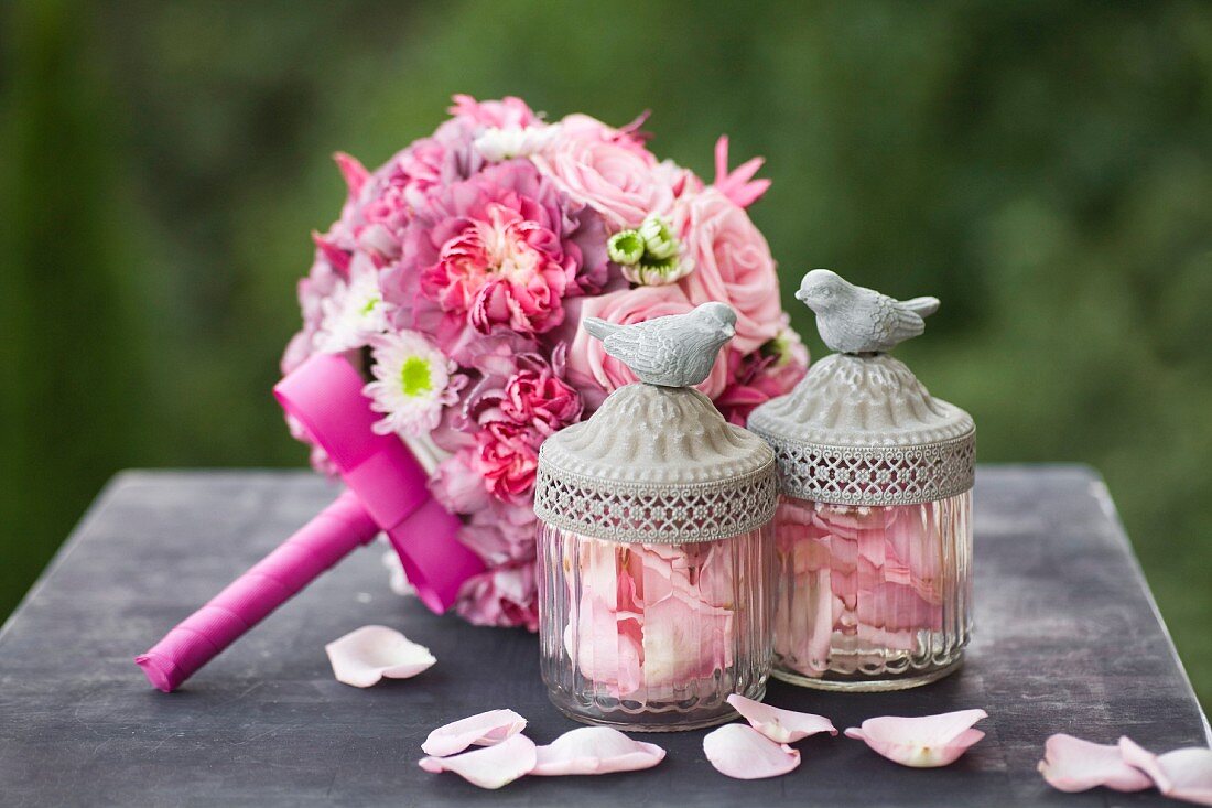 Romantic bridal bouquet with pink roses, scattered rose petals and glass jars with bird figurines on lids
