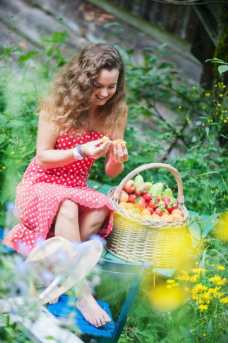 Young woman with basket of fruit in cottage garden (Altenmarkt-Zauchensee, Salzburger Land, Austria)