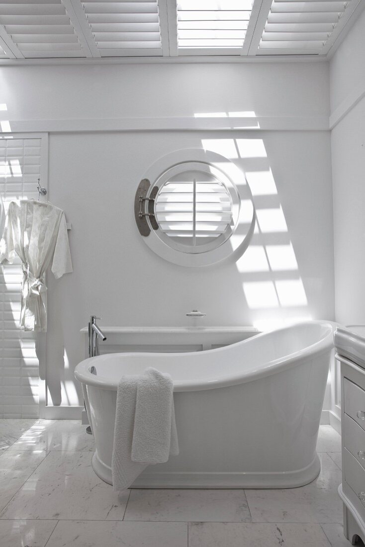 White bathroom with porthole window and vintage-style free-standing bathtub