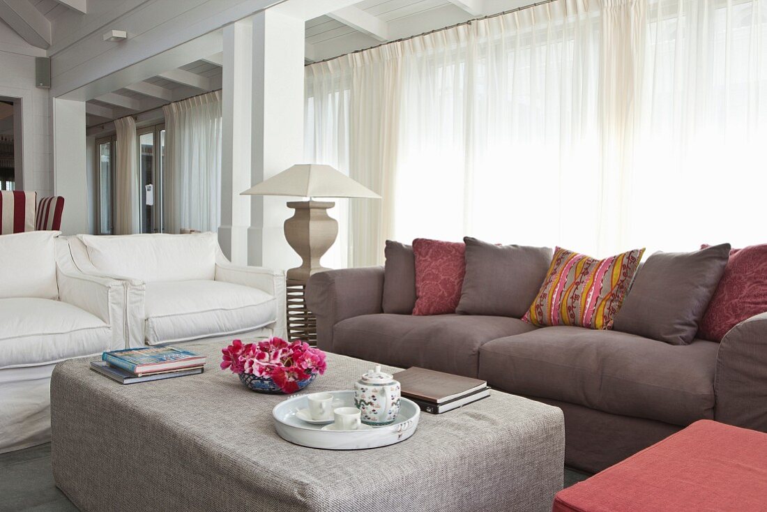 Comfortable elegant living area with upholstered seating, ottoman and white curtains on glass wall