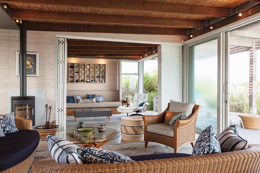 Gemütlicher Loungebereich mit Korbmöbeln, rundem Glastisch und Schwedenofen; Blick auf Terrasse