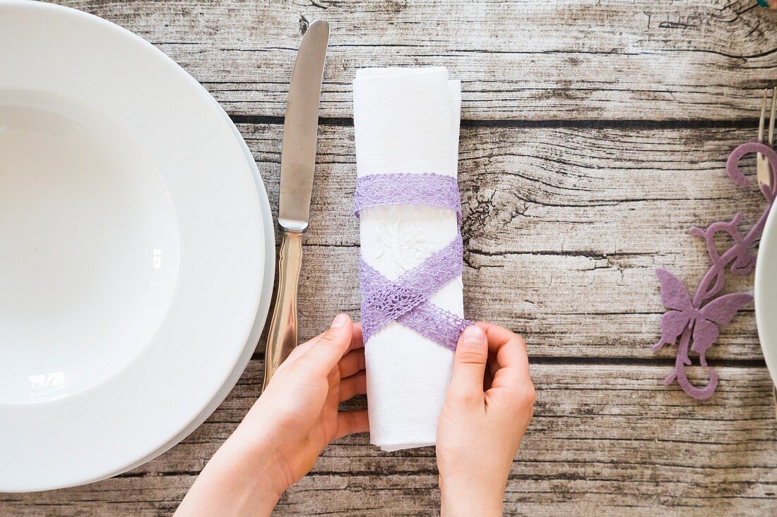 Person decorating linen napkin with purple lace ribbon (top view)