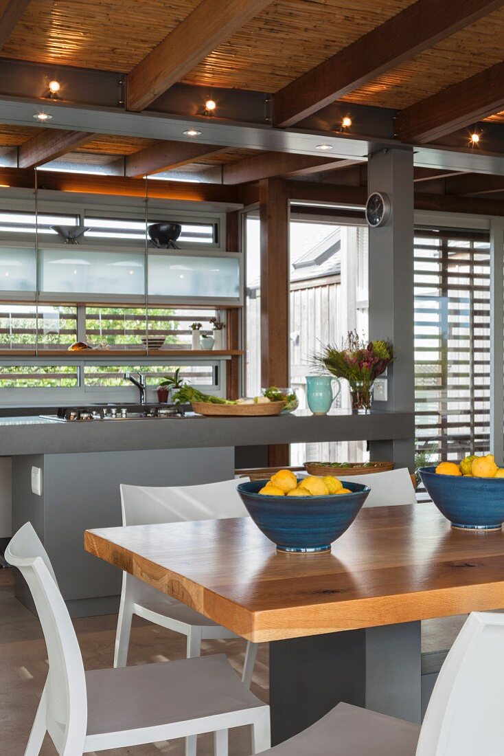 Modern fitted kitchen with island counter, dining table and reed ceiling with wood-beam structure