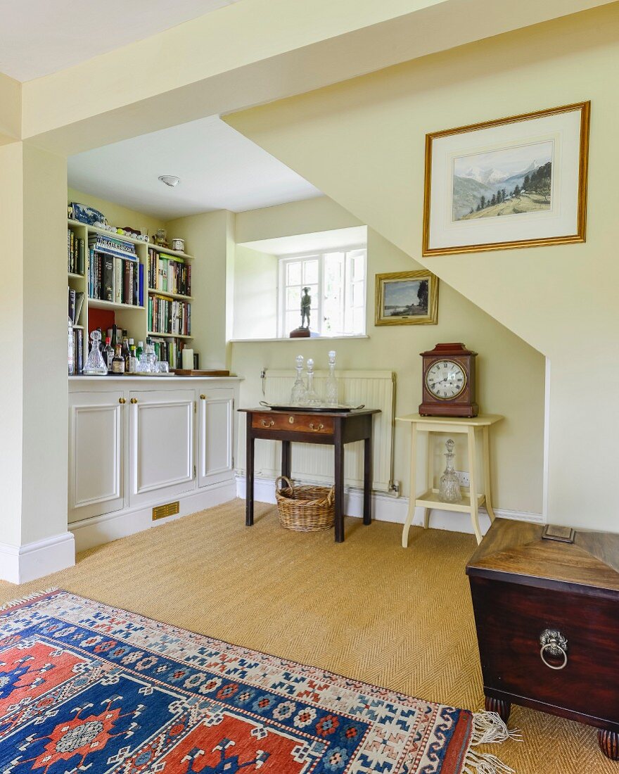 Fitted cabinets and antique furniture in yellow-painted niche under staircase