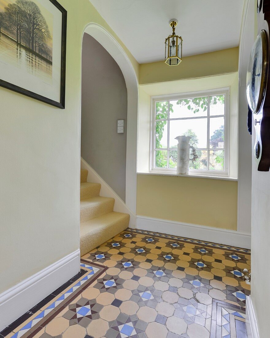 Patterned tiled floor, lattice window and arched doorway over staircase in hallway
