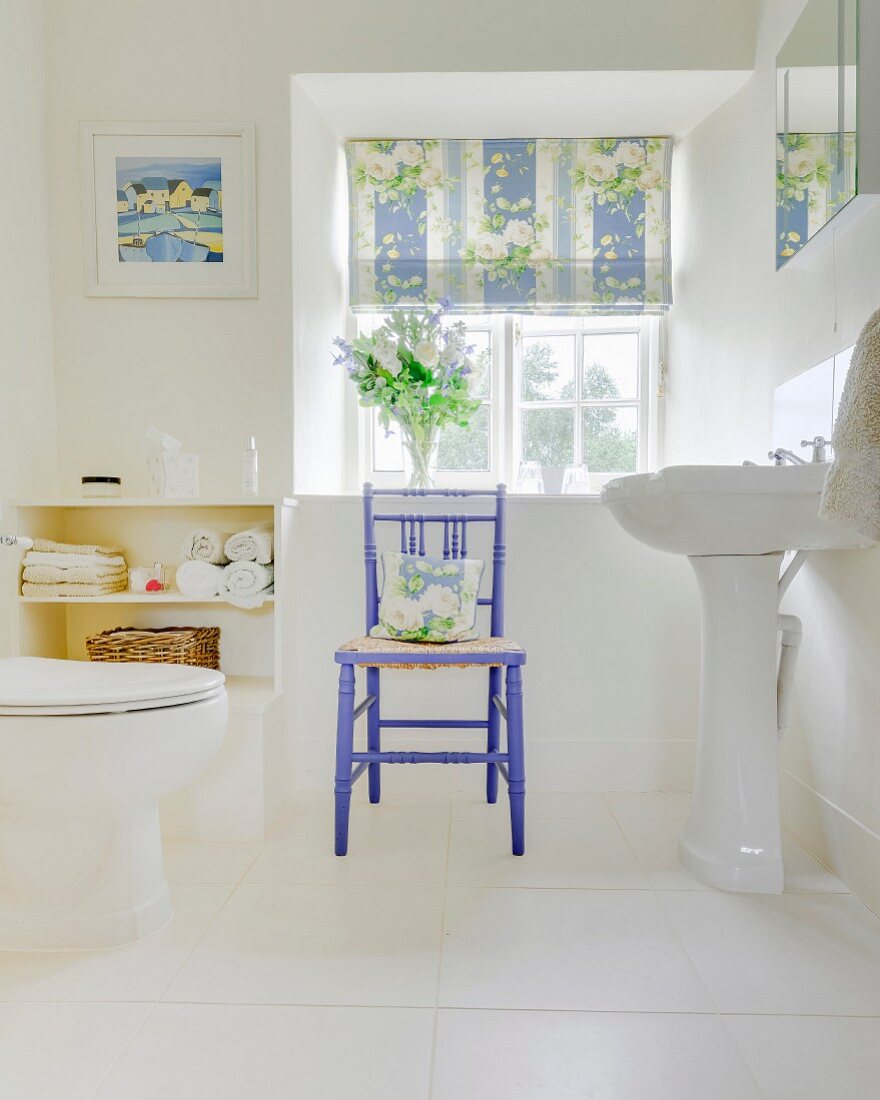 Ländliches Bad mit weißem Fliesenboden, Standwaschbecken und lila lackiertem Holzstuhl vor Sprossenfenster