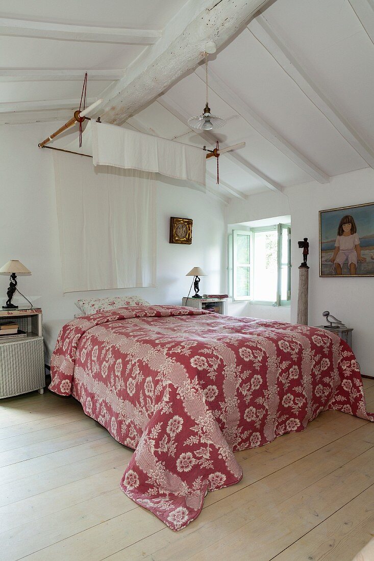 Red and white patterned cover on double bed in bedroom with white wooden ceiling