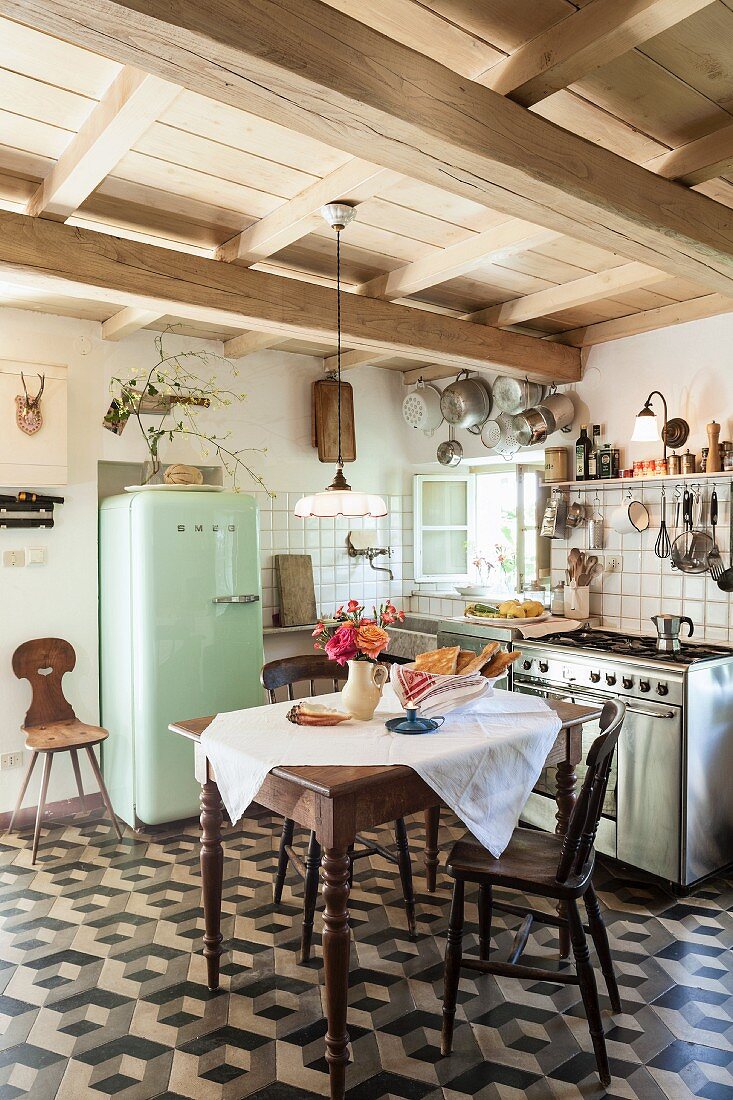 Tisch mit weisser Tischdecke und Holzstühle auf Fliesenboden mit geometrischem Muster in mediterraner Küche