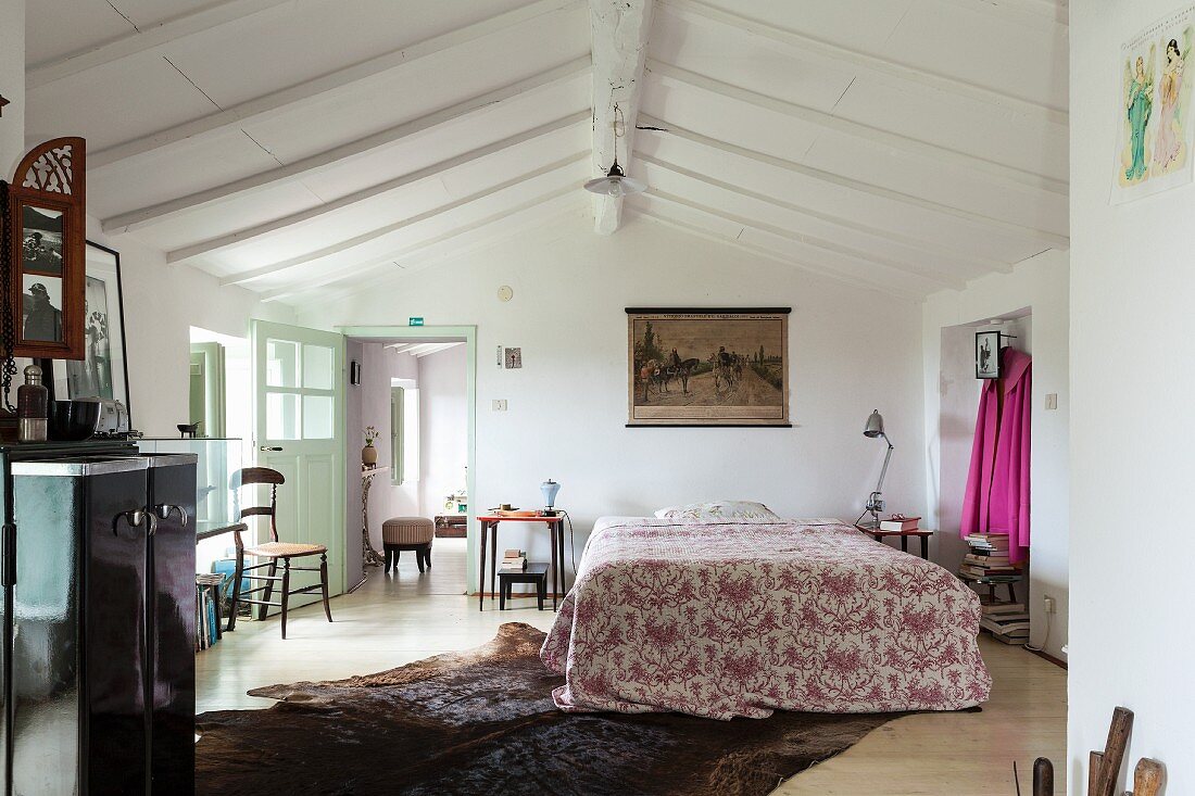 Patterned bedspread on double bed below white wooden ceiling in converted attic