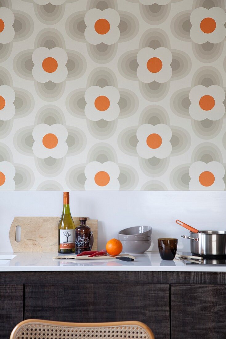 weiße Küchenarbeitsplatte mit Kochutensilien vor Spritzschutz- Streifen und Retro Blumentapete an Wand