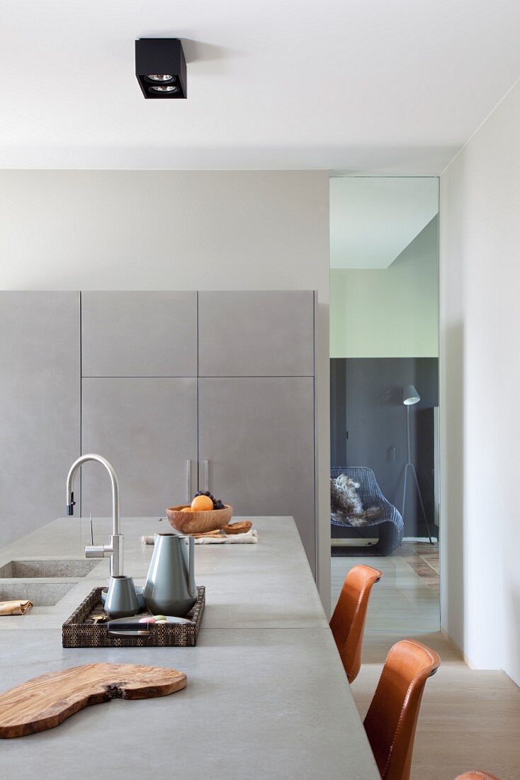 Kitchen counter with concrete worksurface and integrated sink, pale grey fitted cupboards along one wall next to floor-to-ceiling interior window with view into living room
