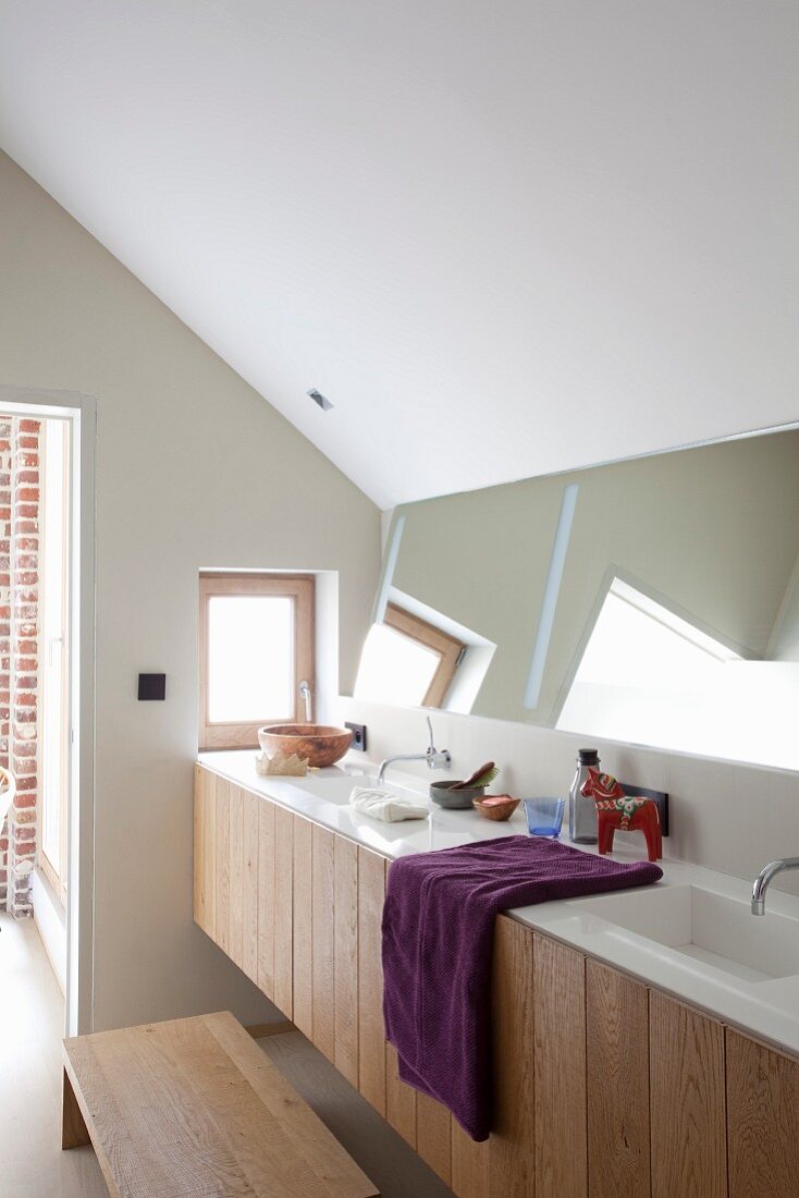 Minimalist washstand with twin sinks below angled mirror on wall under sloping ceiling
