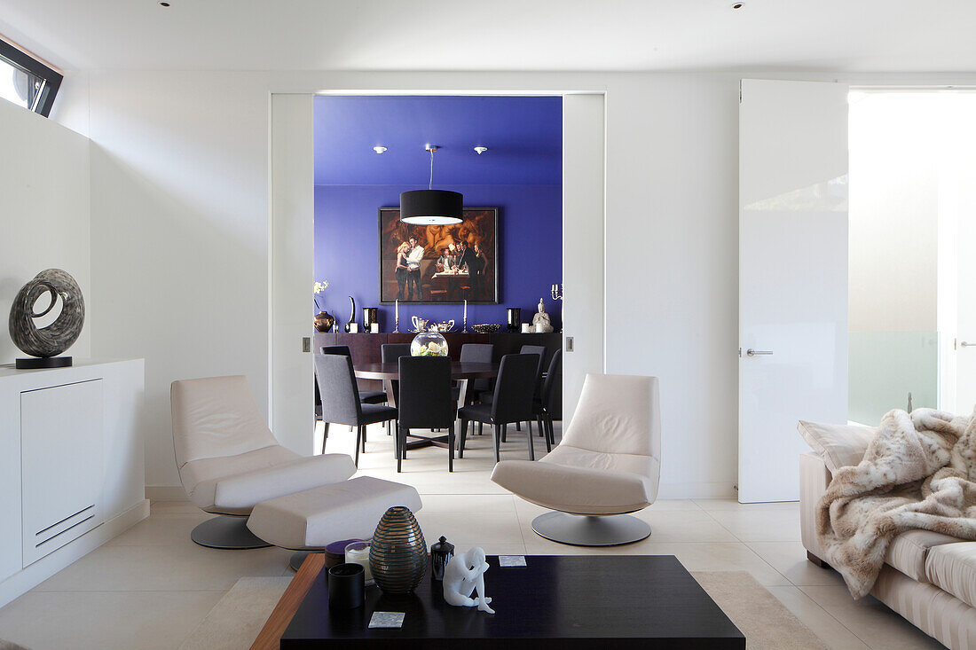 Two designer easy chairs in front of doorway leading into blue dining room