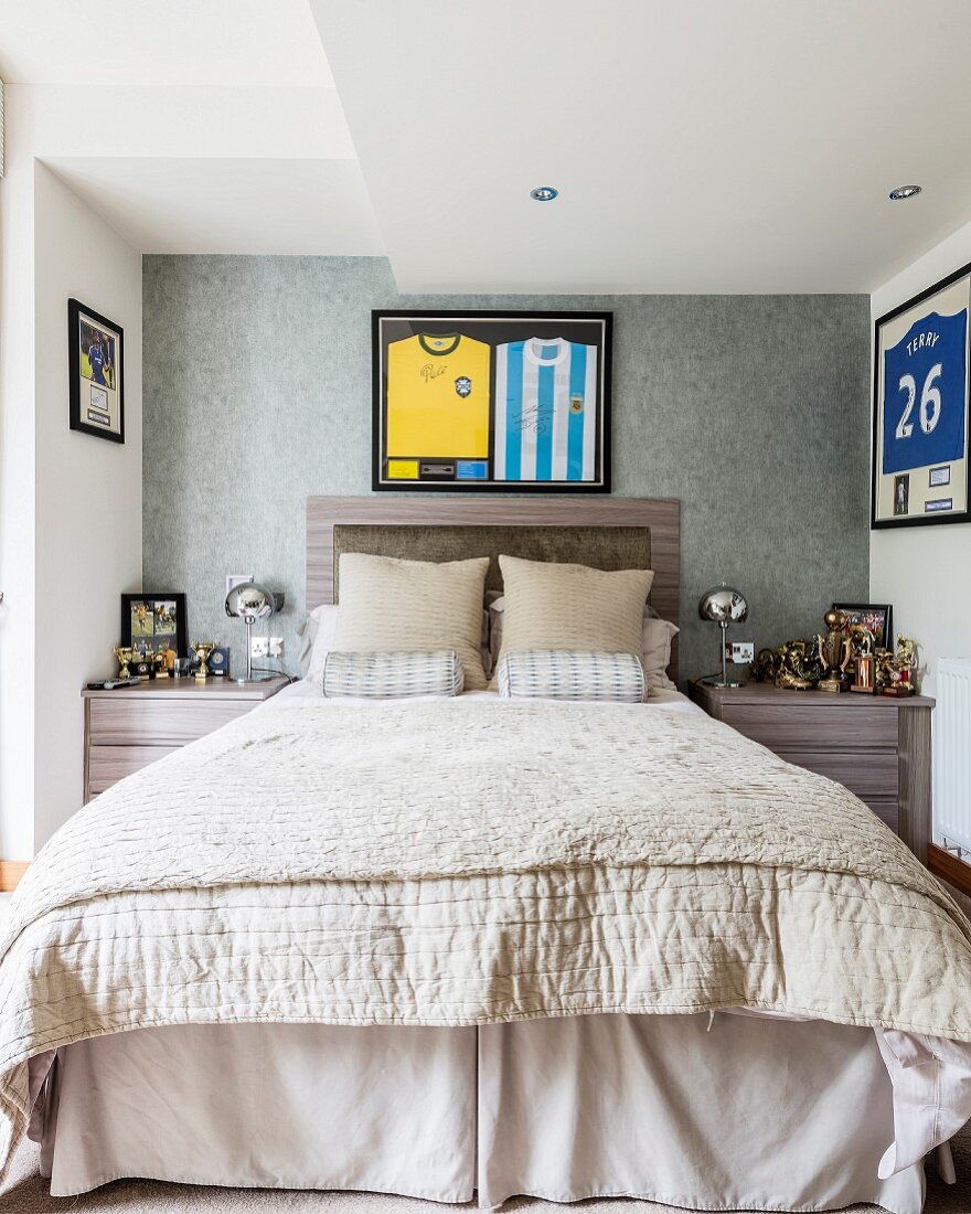 Double bed with headboard below framed sports strips flanked by collection of trophies on bedside tables in elegant bedroom