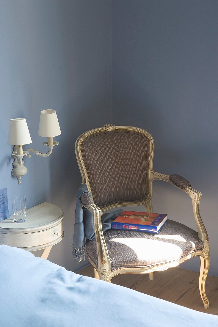 Antique, Rococo-style armchair next to console table on pastel-blue wall