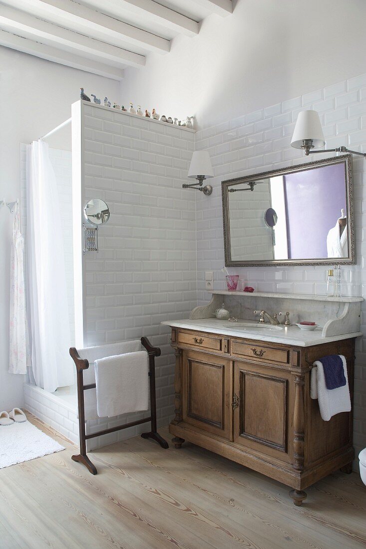 Traditional washstand with marble top next to white-tiled shower partition wall