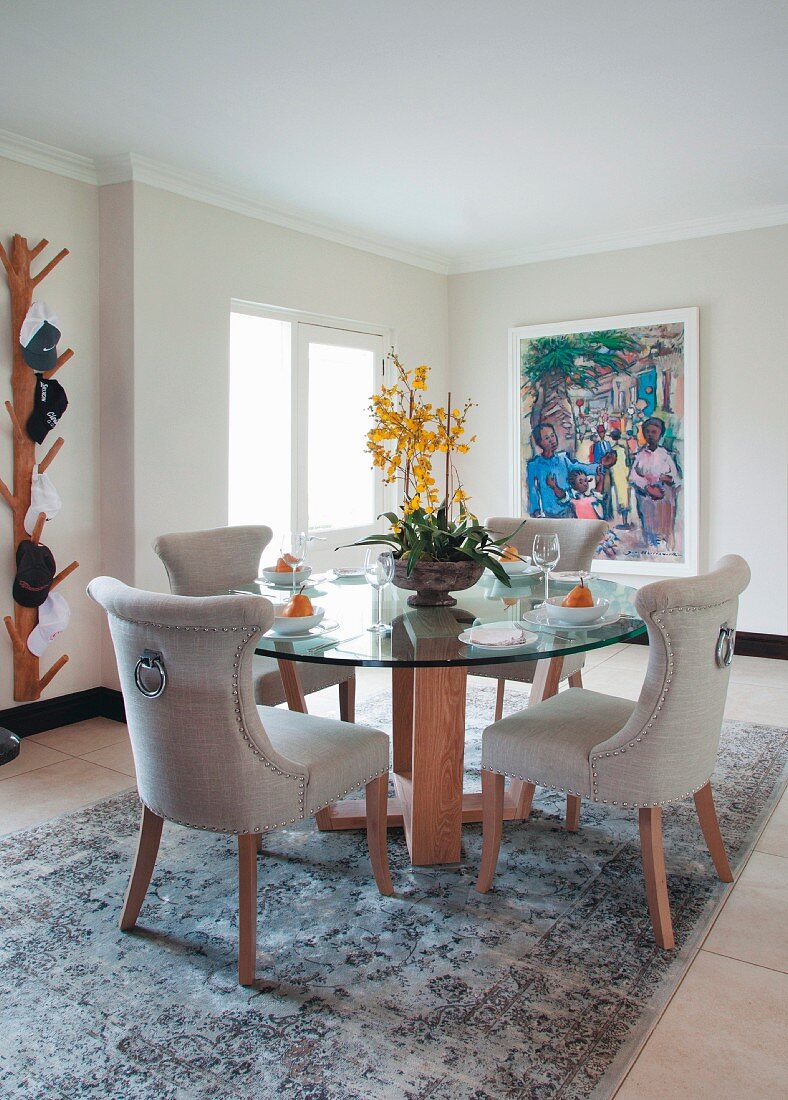 Chairs with pale upholstery at round glass table on rug in dining room with minimalist ambiance