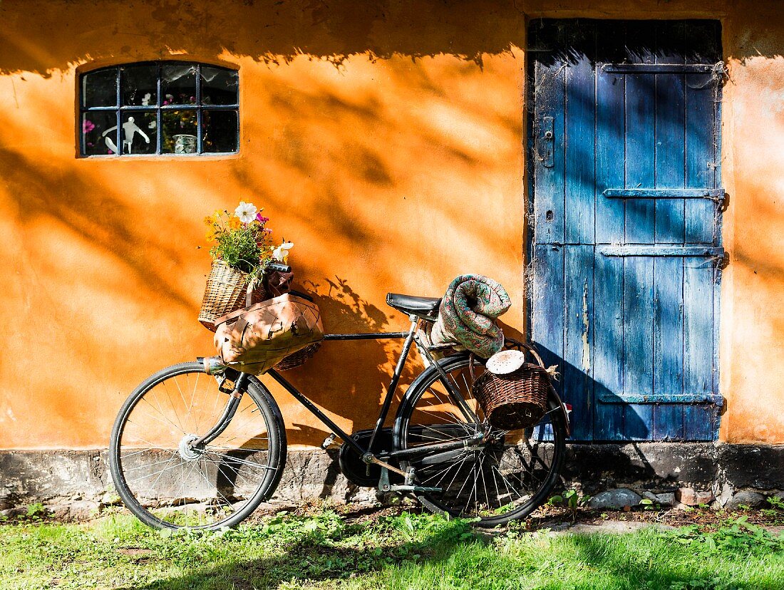 Altes Fahrrad mit Blumenkorb an der orangefarbener Fassade mit blauer Holztür