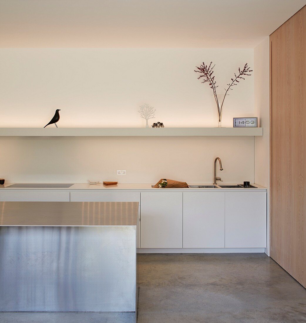White minimalist kitchen with a few ornaments on floating shelves and floor-to-ceiling wooden sliding door