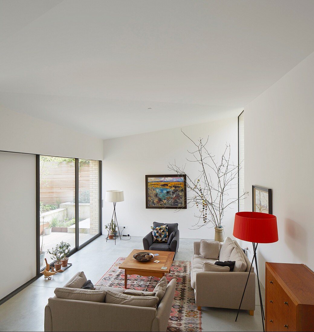 Blick von Galerie auf gemütlichen Wohnbereich mit beigefarbenen Polstermöbeln und Stehleuchte mit rotem Lampenschirm