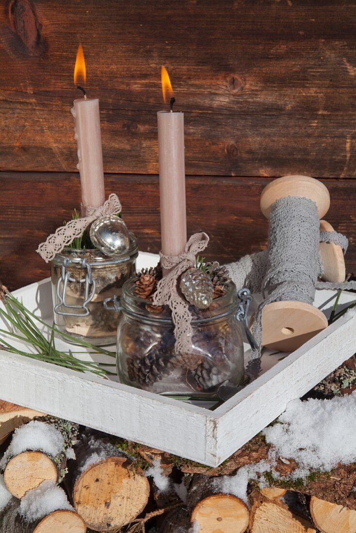 Adventsdekoration vor rustikaler Holzwand mit zwei brennenden Kerzen in nostalgischen Einmachgläsern