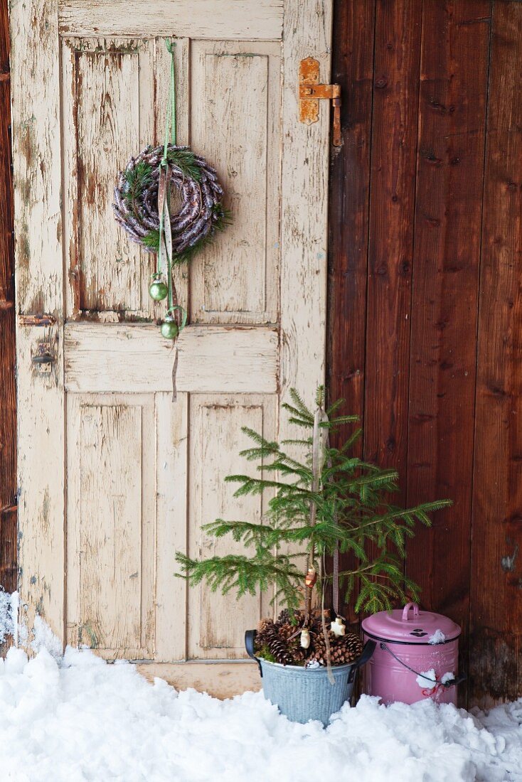 Wreath of pine cones and small Christmas tree in front of old door