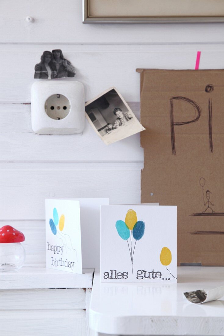 Selbstgebastelte Geburtstagskarten mit Luftballon-Motiven vor weißer Holzwand mit schwarz-weiß Foto