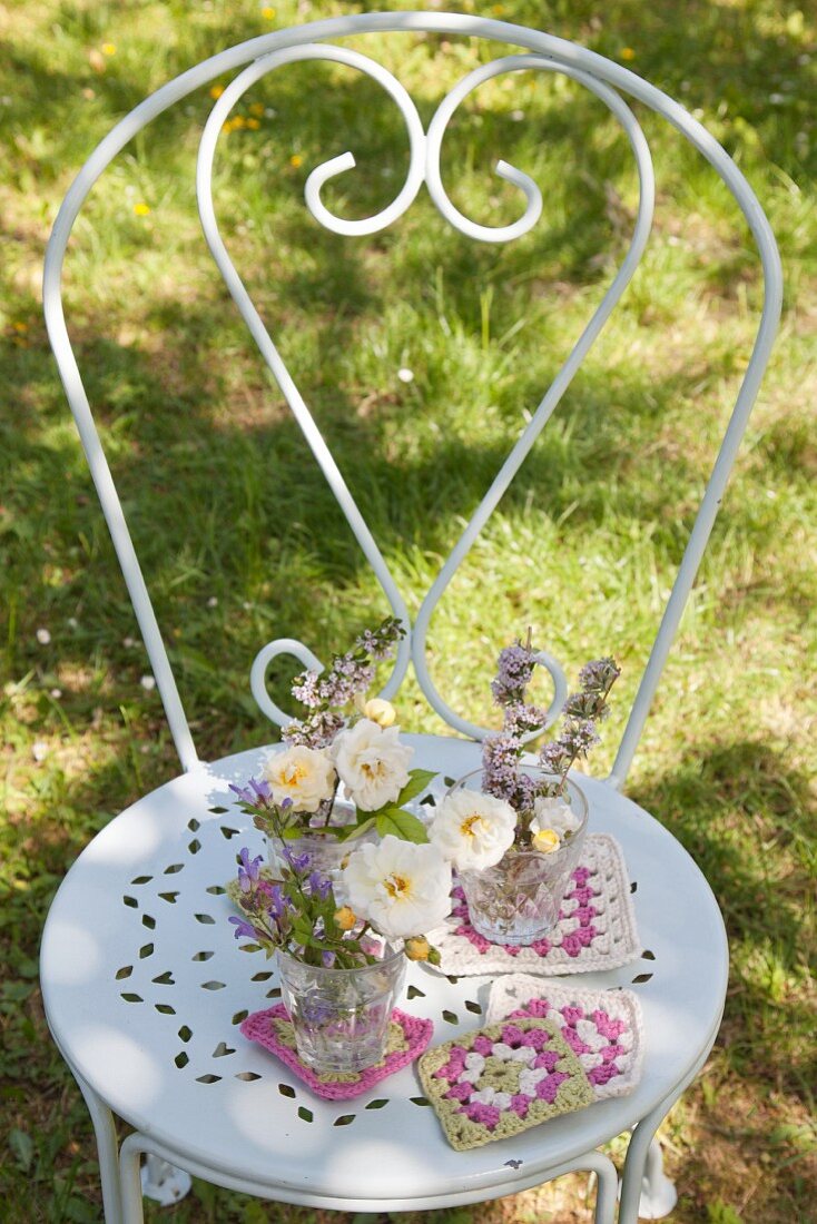 Blumensträußchen mit gehäkelten Untersetzern auf weißem Metallstuhl im Garten