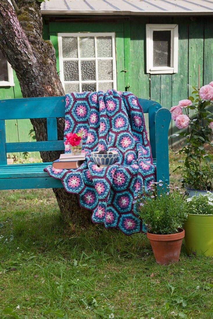 Crocheted blanket with hexagonal pattern in shades of blue and purple on garden bench in front of cabin