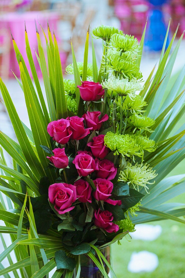 Festliches Gesteck aus pinkfarbenen Rosen mit Palmenblättern umwickelt