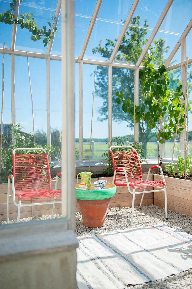 Red garden chairs and small table made from terracotta pot in conservatory with gravel floor