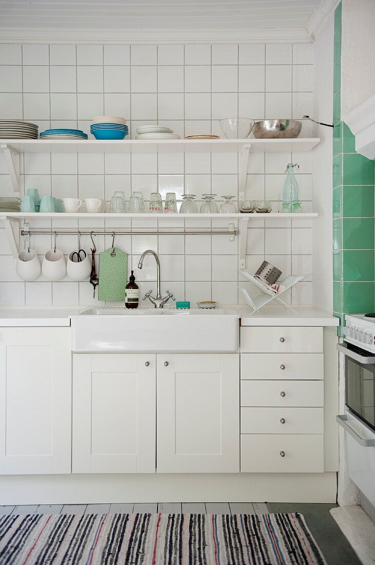 Sink on white base units below tiled wall and bracket shelves in kitchen