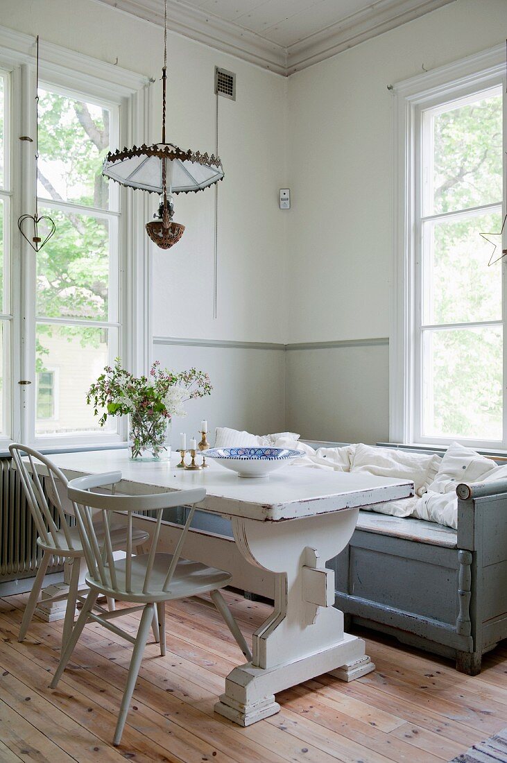 Essplatz mit hellgrauen Stühlen an weißem Vintage Tisch und Sitzbank vor Fenster