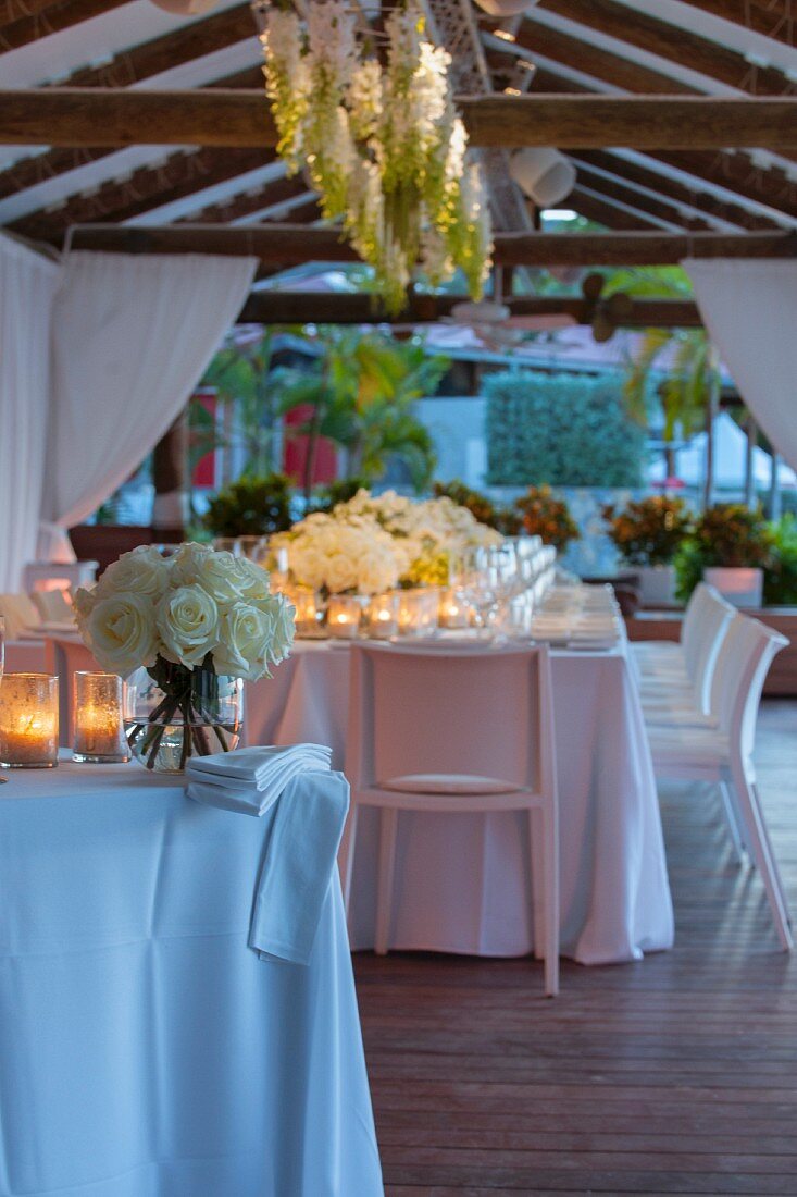 Wedding dinner table festively decorated with candle lanterns and bouquets on roofed terrace