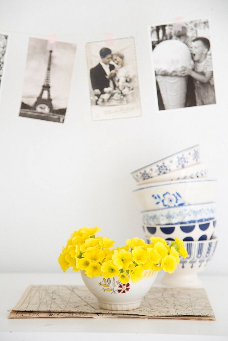 Gelbe Primelblüten in Vintage-Schale vor Postkarten und gestapelten Schalen