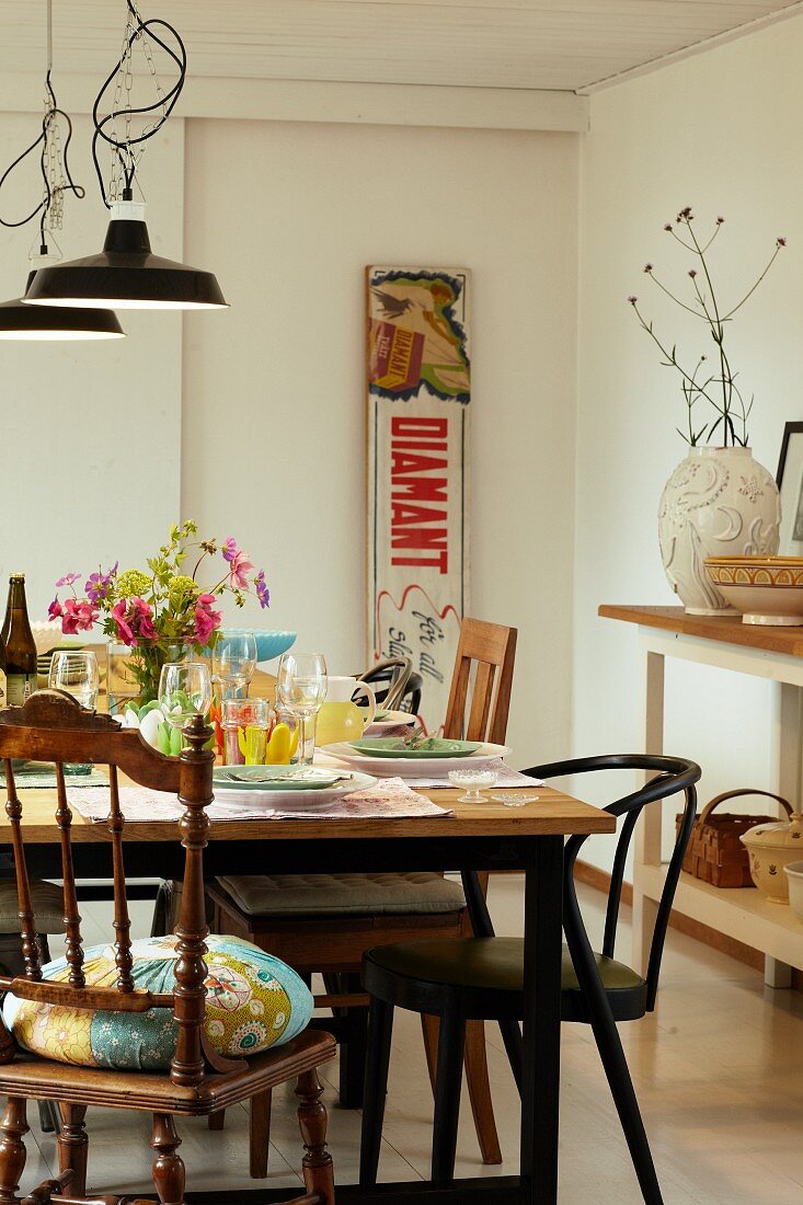 Gedeckter Tisch mit unterschiedlichen Stühlen, Vintage-Dekoschild und offenem Regal mit Landhaus-Flair