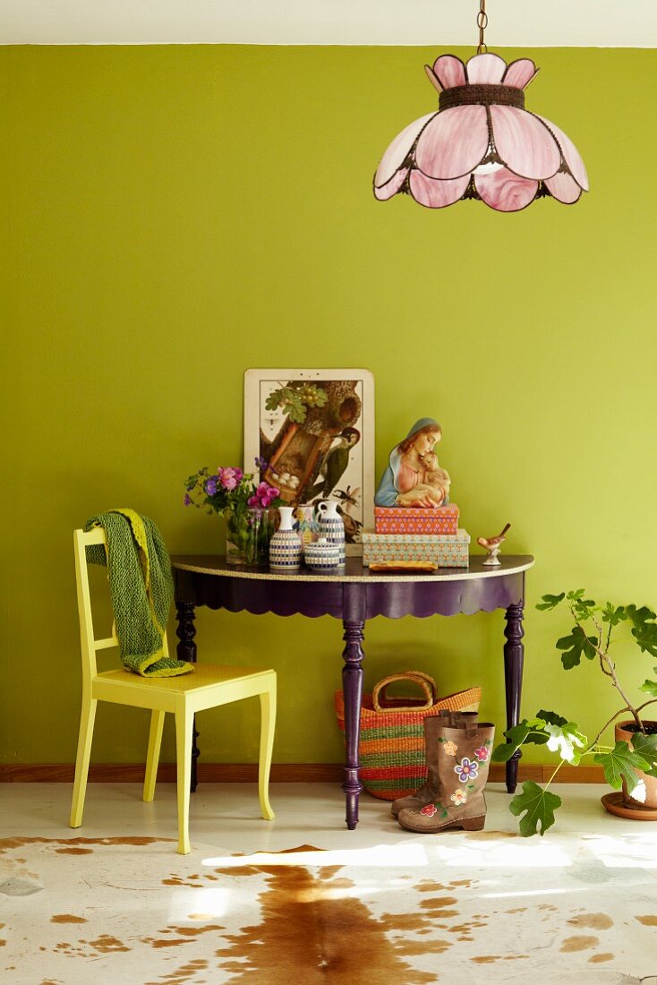 Ornaments on console table painted purple and yellow wooden chair against lime green wall in colourful, eclectic interior