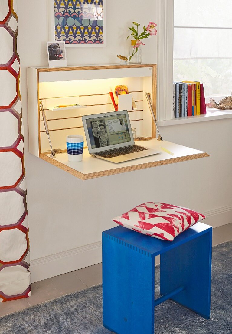 Schlichtes Hängeschränkchen mit klappbarer Multiplex-Schreibtischplatte, indirekter Beleuchtung und Laptop