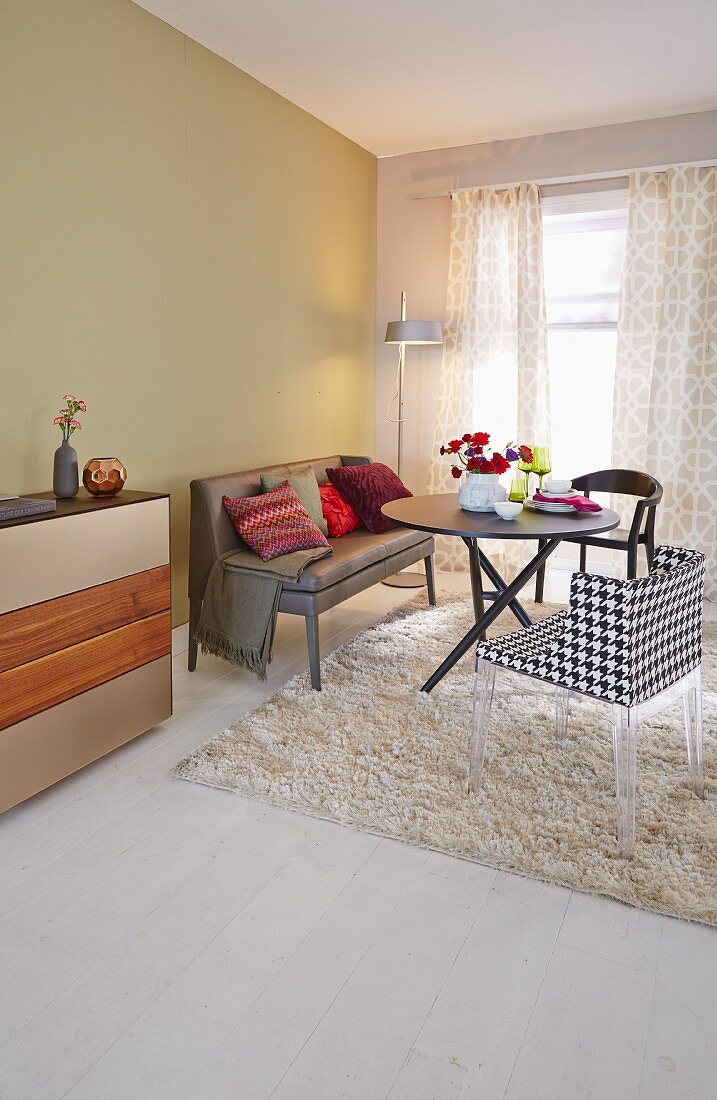 Stilvoller reduzierter Wohnbereich mit pastellgrüner Wand, gemütlicher Lederpolsterbank, rundem Tisch und Plexiglasstuhl