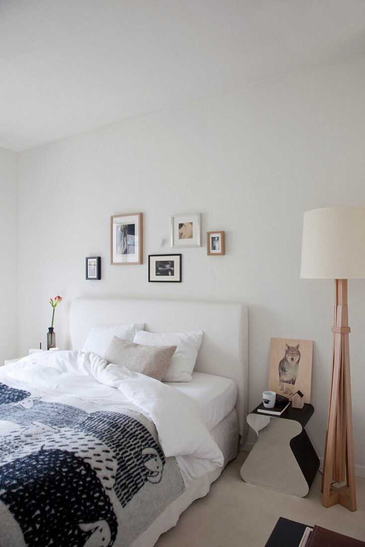 Sheep-patterned bedspread on double bed with white headboard, bedside table and standard lamp