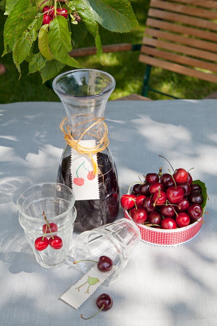 Karaffe mit gebasteltem Etikett, Gläser und eine Schale mit Kirschen