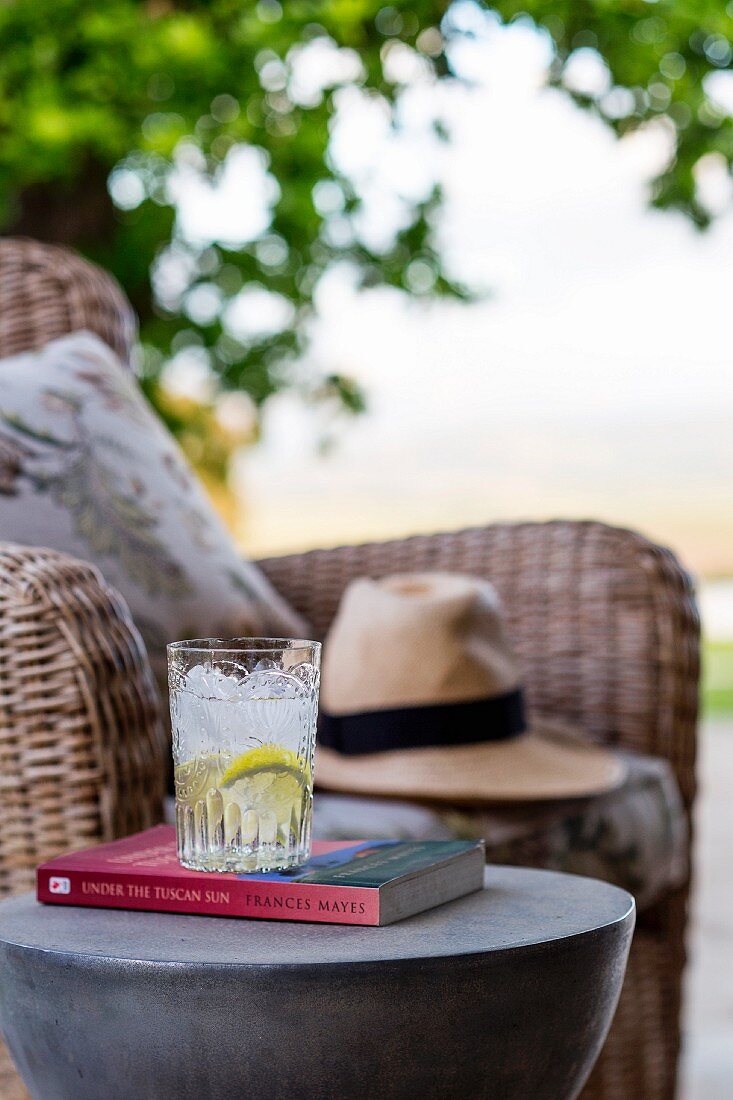 Refreshing drink on book on side table next to wicker armchair outdoors