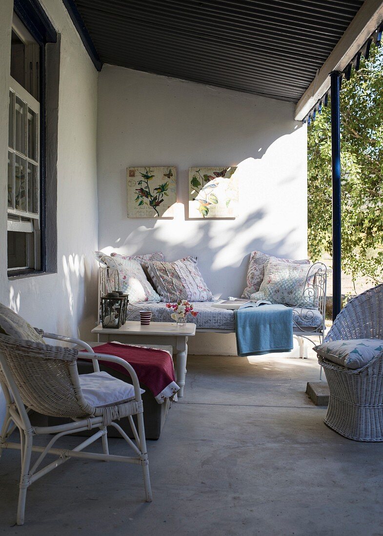 Gemütlicher Sitzplatz auf Veranda mit weißen Korbmöbeln und traditionellem Flair