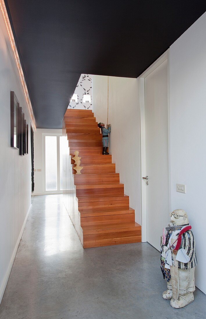 Wooden staircase, concrete floor and sculptures in modern hallway